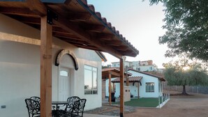 Un patio con mesa y sillas, un área cubierta con pérgola, y una casa de fachada blanca y césped verde.