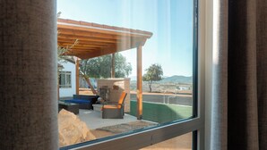 Vista desde una habitación con un ventanal grande que da a un patio con mobiliario exterior y una pérgola.
