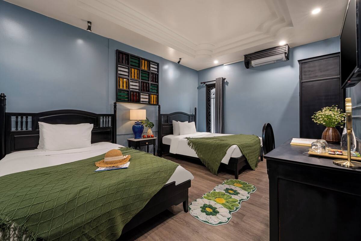 Ein Hotelzimmer mit zwei Betten, einem Schreibtisch, einem Bücherregal und einer Klimaanlage.