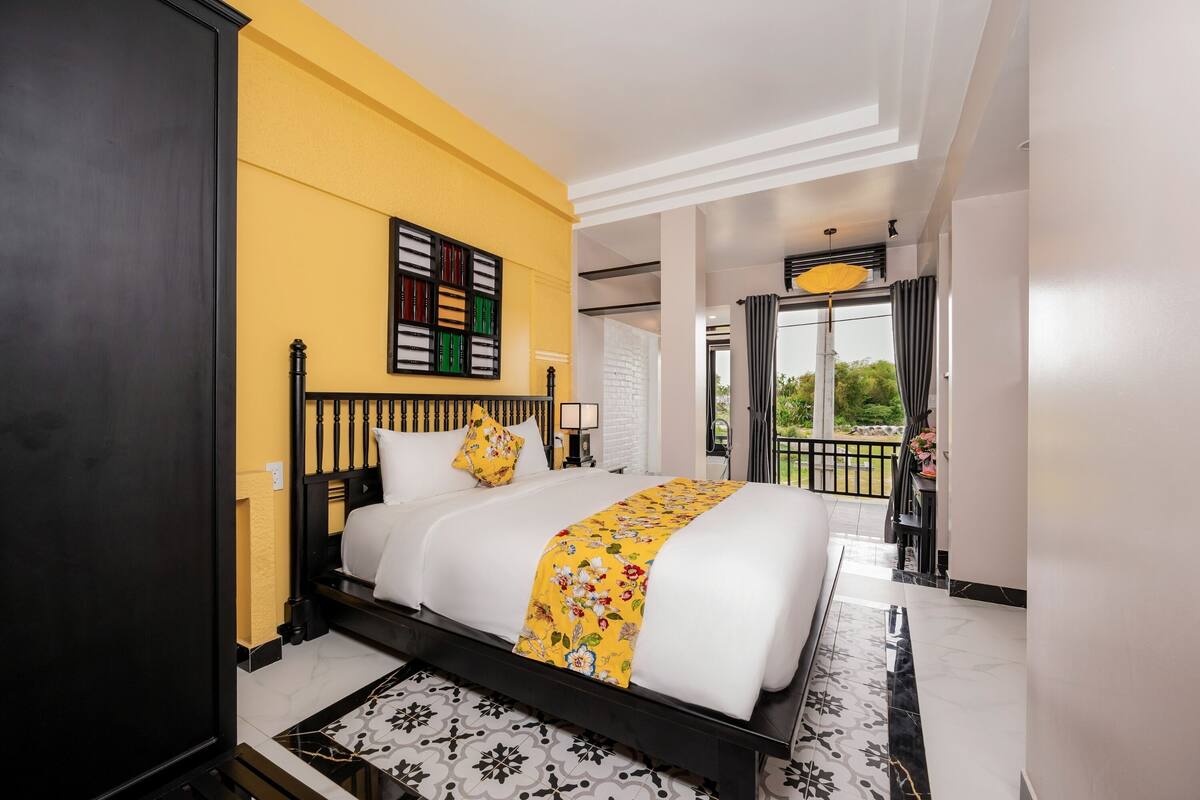 Ein Hotelzimmer mit Bett, einer gelben Wand, einem Fenster mit Blick und einem Balkon.