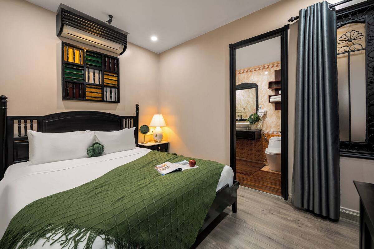 Ein Hotelzimmer mit einem Bett, einem Nachttisch mit Lampe, einem Spiegel und einem durch eine offene Tür einsehbarer Badezimmer.