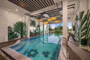 Una piscina interior con baldosas hexagonales, rodeada de paredes de ladrillo blanco y grandes murales con hojas verdes.