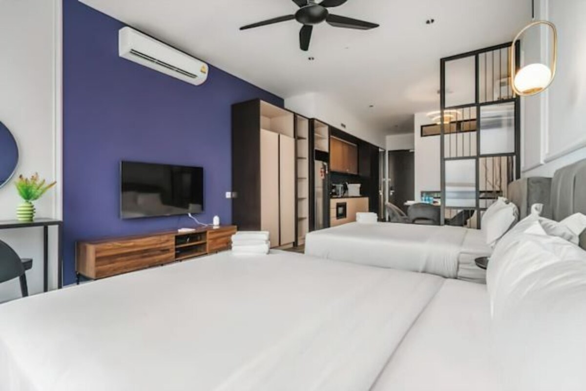 Een moderne hotelkamer met een groot bed, een televisie, een plafondventilator en een kitchenette.