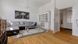 A modern living room with a sofa, a glass coffee table, a chandelier, and a staircase leading to another level. - Apartment 'Am Herforder Tor Für' with Private Garden, Balcony and Wi-Fi (Bad Salzuflen)