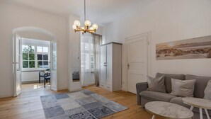 A living room with a sofa, a round table, a chandelier, a large window, and a painting on the wall. - Apartment 'Am Herforder Tor Für' with Private Garden, Balcony and Wi-Fi (Bad Salzuflen)