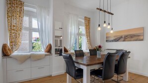 A dining area with a wooden table, black chairs, and a view of the outdoors through large windows. - Apartment 'Am Herforder Tor Für' with Private Garden, Balcony and Wi-Fi (Bad Salzuflen)