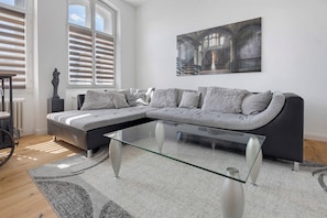 Ein modernes Wohnzimmer mit einem modularen Sofa, einem Glastisch und einem großen Gemälde an der Wand.