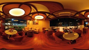 A restaurant with round tables and red chairs, a wooden floor, and a view of the city at night. - Hotel Q Green (Nalbari)