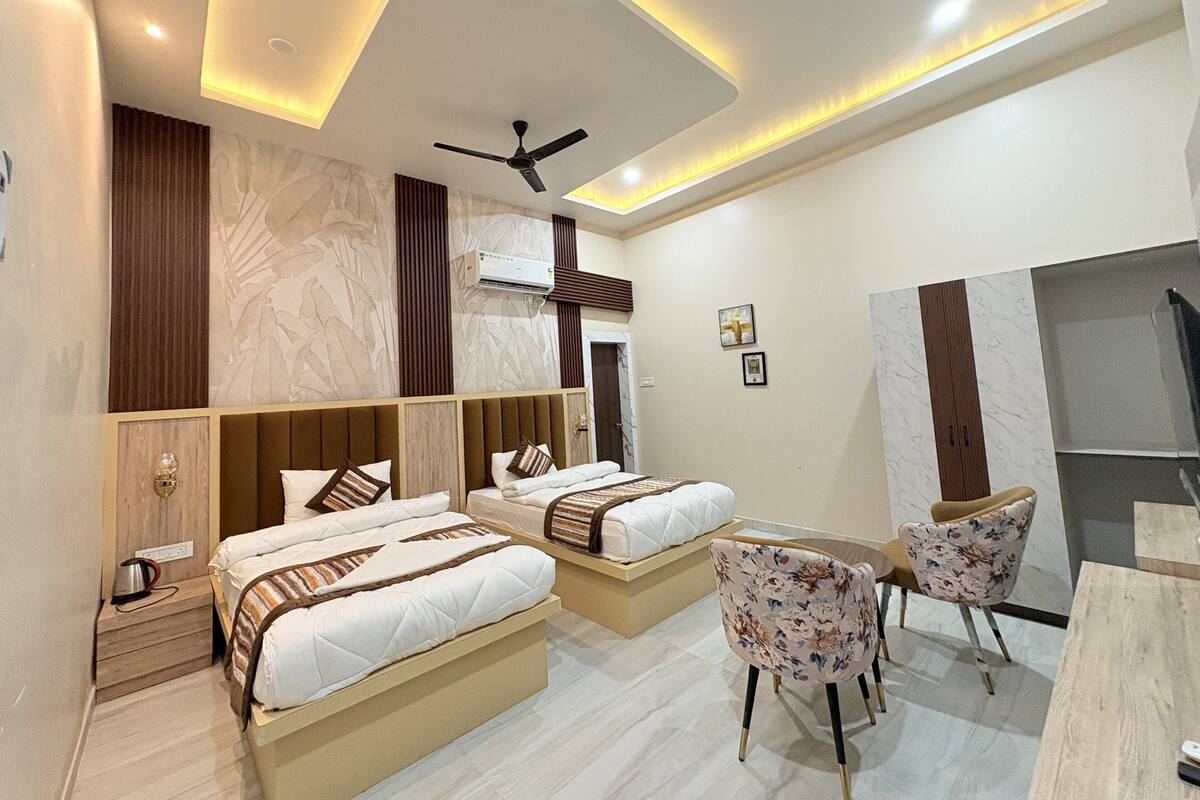 A modern hotel room with two beds, a ceiling fan, a seating area with chairs, and a large window.