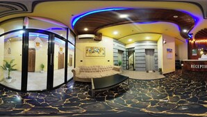 A hotel lobby with a reception desk, a round seating area, and a glass partition with artwork. - Hotel Q Green (Nalbari)