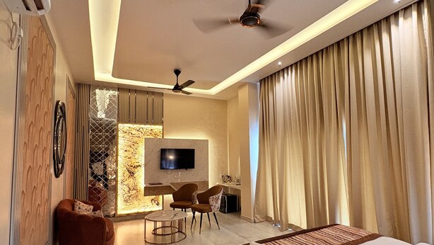 A modern hotel room with a large bed, a seating area with chairs, a TV, and a ceiling fan. - Hotel Q Green (Nalbari)
