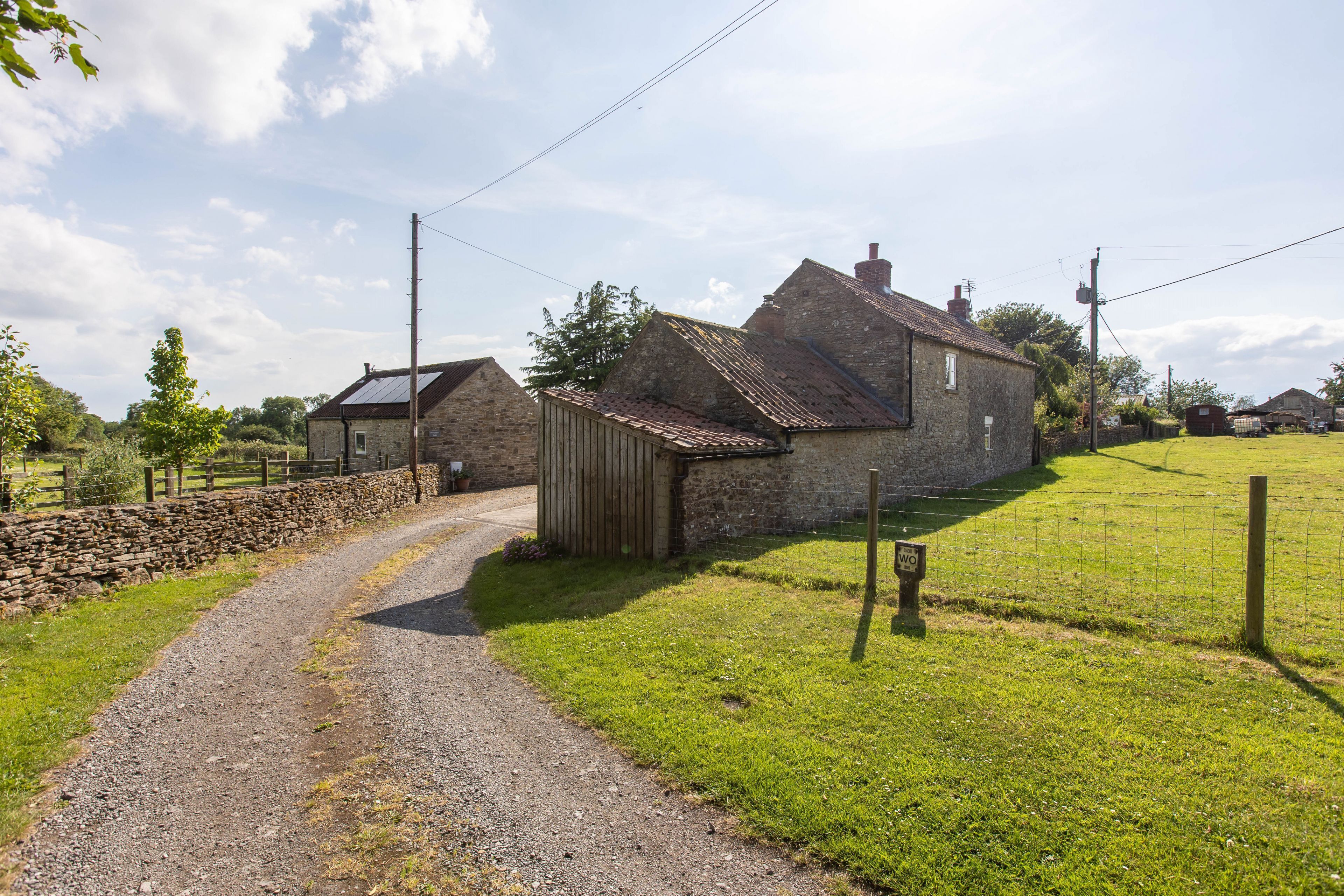A rural setting with a stone house, a gravel path, and a fenced area.