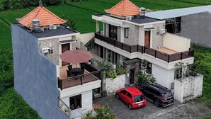 A modern two-story house with a red car parked in the driveway, surrounded by lush greenery and a clear sky. - Jnana Bali Villa (Sukawati)