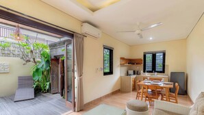 A modern living area with a dining table, sofa, and a small balcony with a plant. - Jnana Bali Villa (Sukawati)