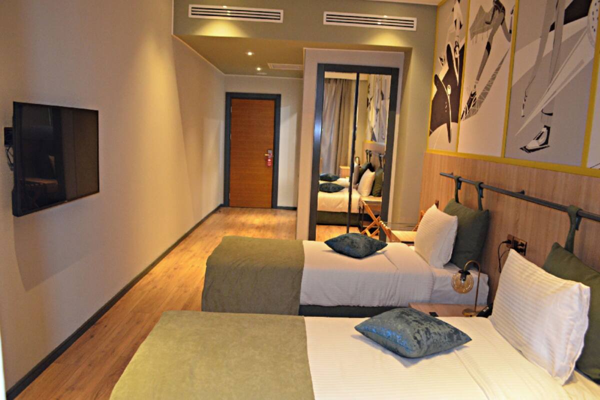 A hotel room with two beds, a TV, a mirror, and a door leading to a bathroom.