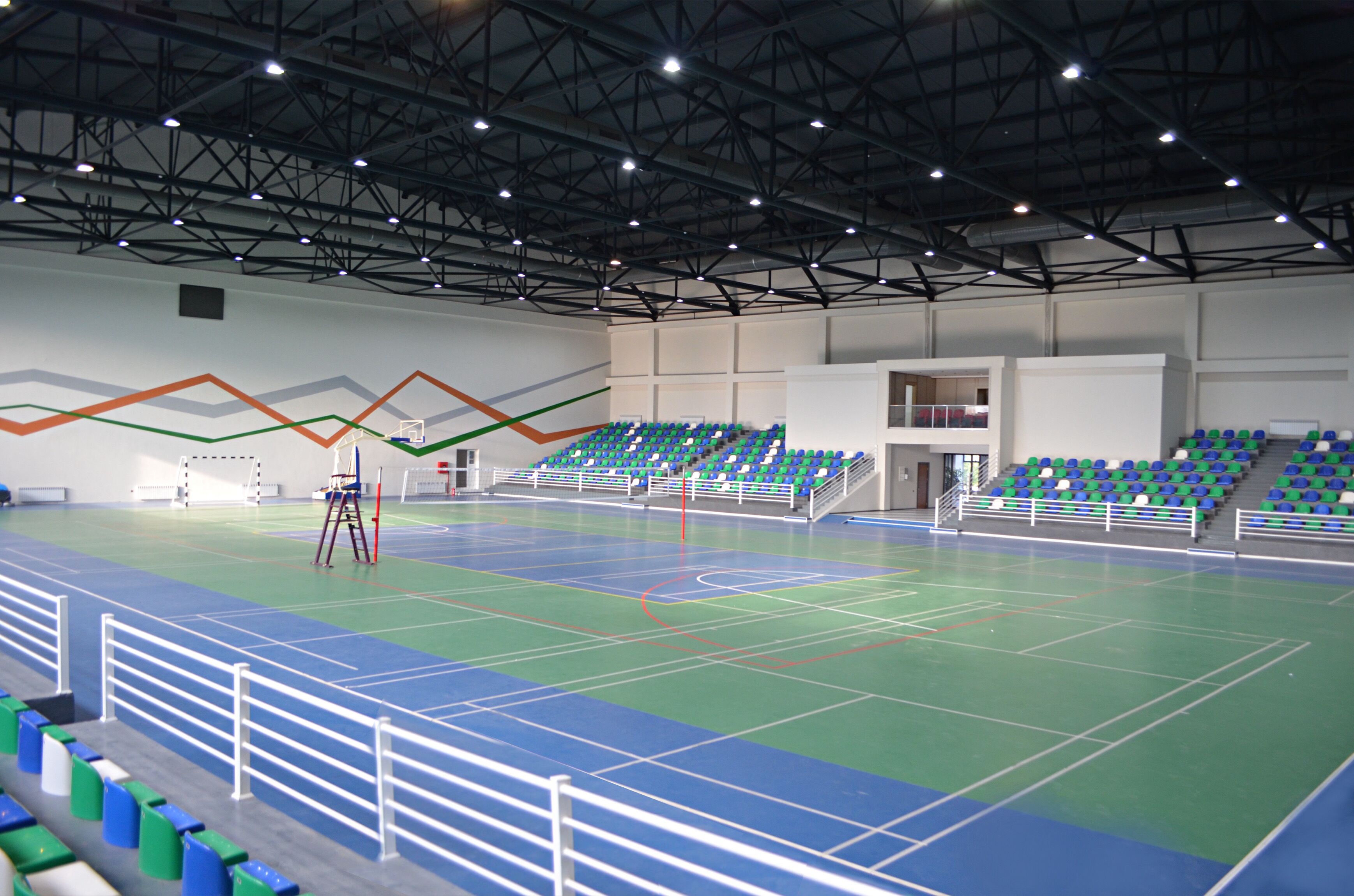 An indoor sports hall with multiple seating areas, a basketball court, and a climbing wall.
