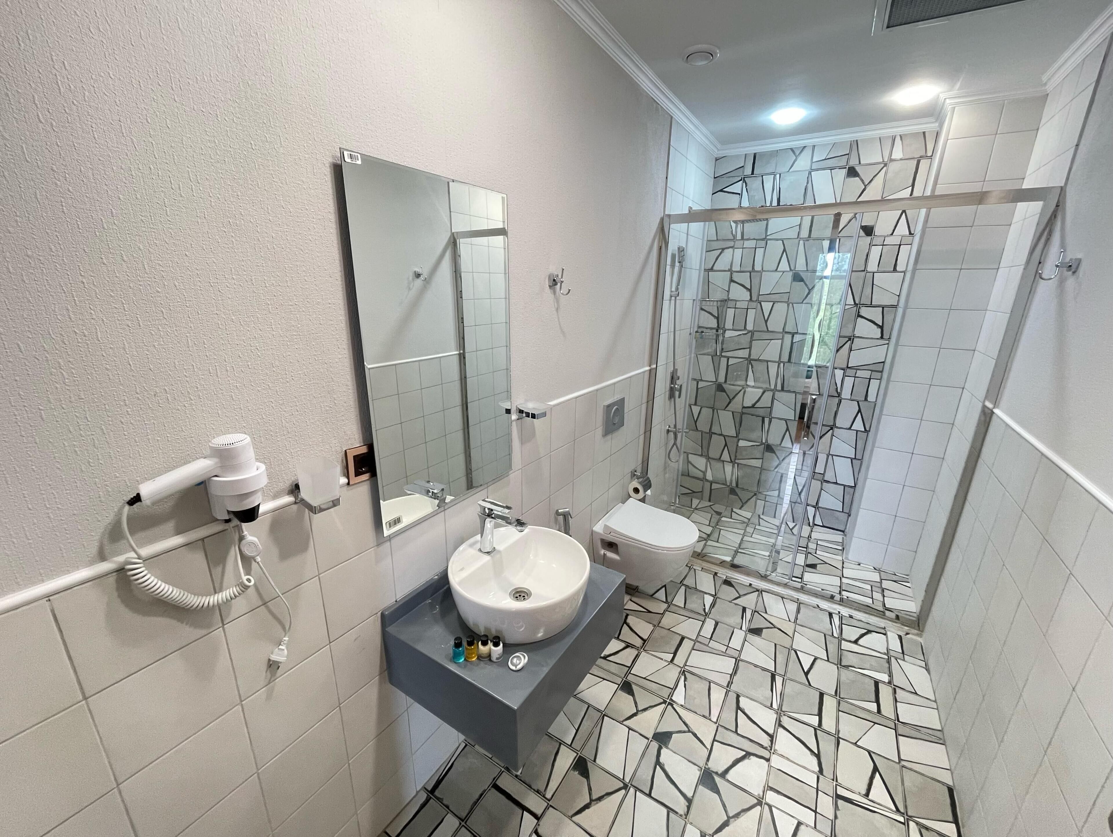 Un baño con lavamanos blanco, espejo y ducha con puerta de cristal.