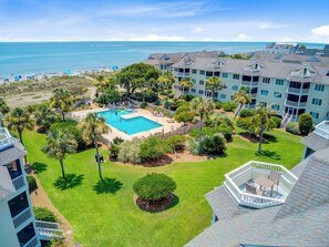 Um resort com piscina central, vegetação exuberante e vista para a praia.