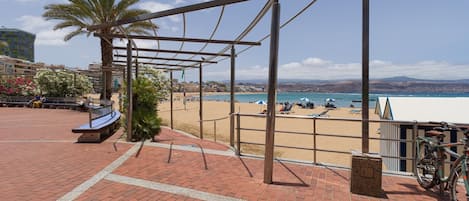 Um calçadão à beira-mar com uma pérgula de metal, um banco e uma bicicleta.