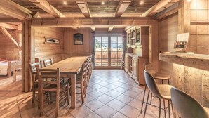 Un intérieur en bois comprenant une table à manger, des chaises, un coin cuisine et une vue à travers une porte vitrée.