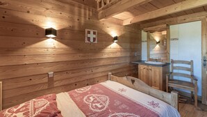 L’intérieur d’un chalet en bois comprend un lit, une chaise en bois, un petit bureau avec un miroir et une porte.