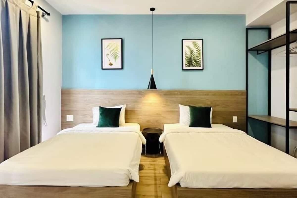 A hotel room with two beds, a wooden headboard, a blue wall, and two framed leaf paintings.