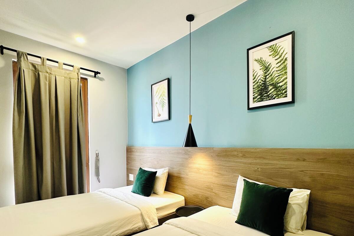 A hotel room with two beds, a wooden headboard, a hanging pendant light, and two framed pictures on the wall.