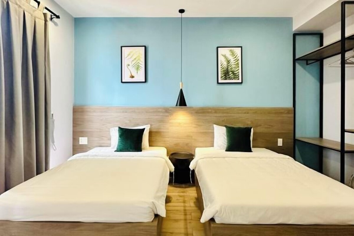 A hotel room with two beds, a wooden headboard, a blue wall, and two framed leaf paintings.