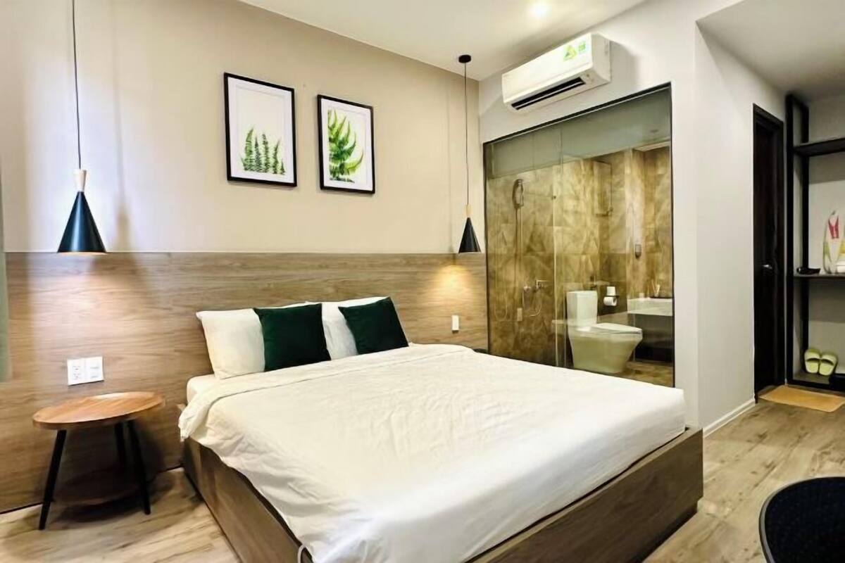 A modern hotel room with a large bed, a small side table, a mirror, and a shower area.