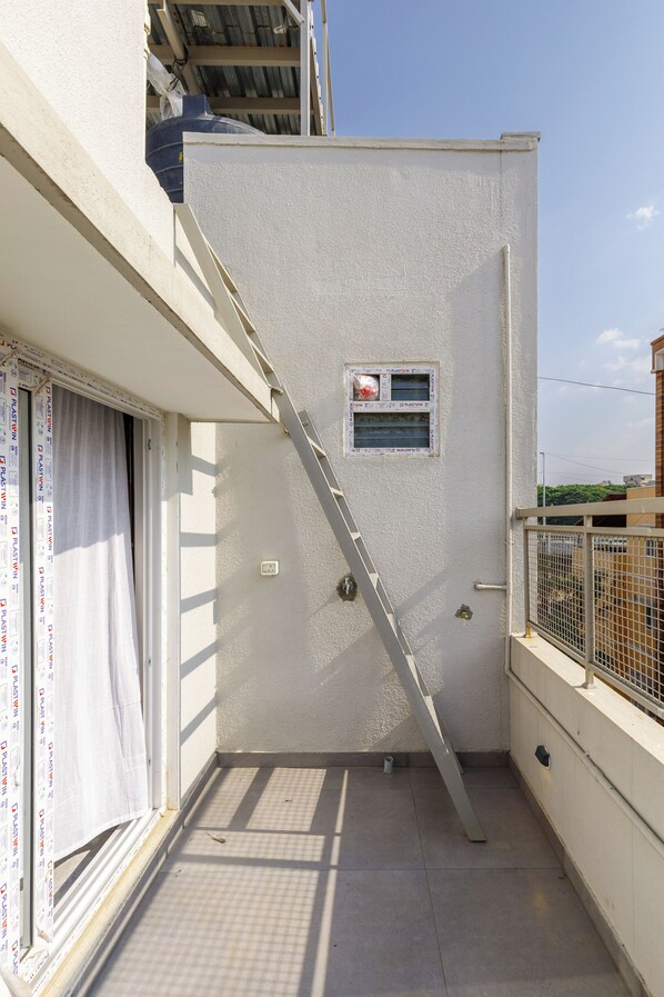Un pequeño balcón con una escalera metálica, una ventana con vista al cielo y una puerta blanca.