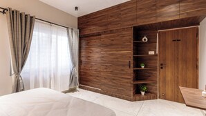 A bedroom with a large bed, a wooden accent wall, a wardrobe, and a small shelf with plants. - The Monarch Stay by Red Olive (Bengaluru)