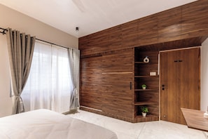 A bedroom with a large bed, a wooden accent wall, a wardrobe, and a small shelf with plants. - The Monarch Stay by Red Olive (Bengaluru)