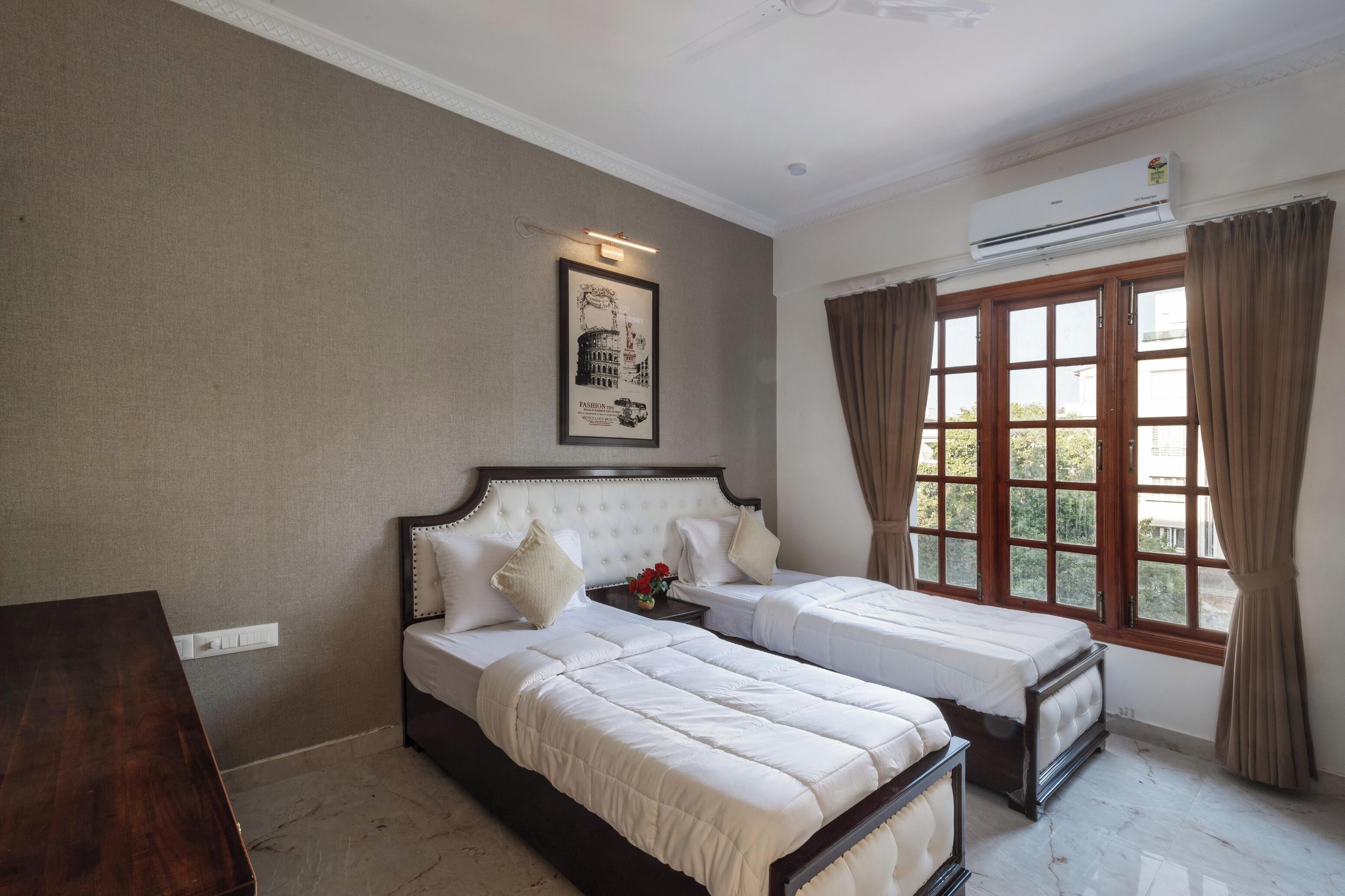 A hotel room with two beds, a wooden nightstand, a framed picture on the wall, and a window with curtains.