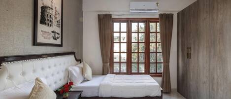 A hotel room with two beds, a large framed picture on the wall, an air conditioning unit, and a window with curtains.