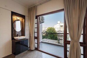 A modern bathroom with a large mirror, a sink, and a balcony with a view of the city. - Avalon Apartments (Bengaluru)