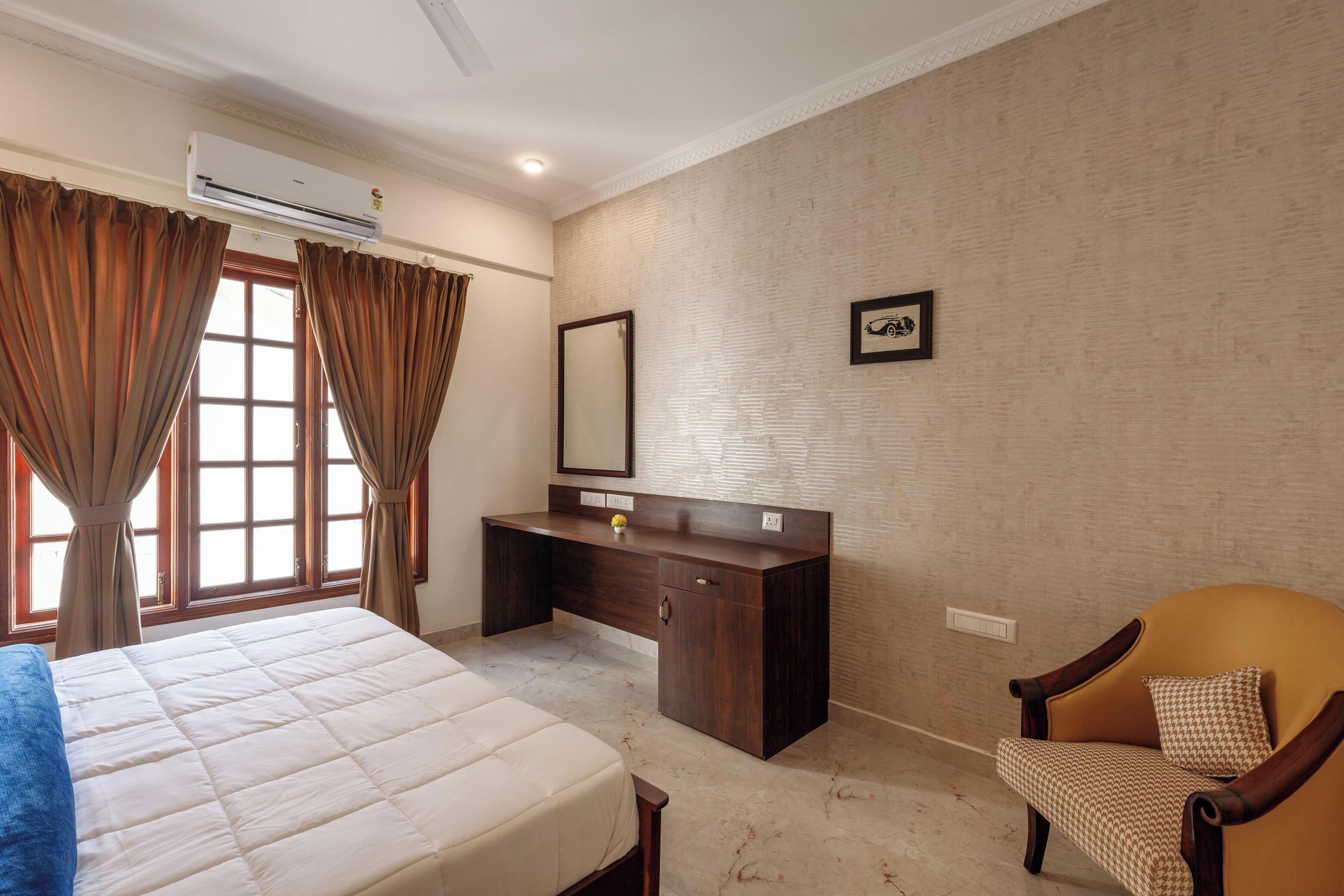 A bedroom with a bed, a desk, a chair, and a large window with curtains.
