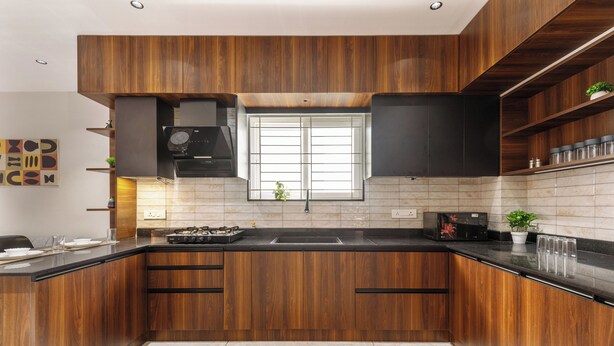 A modern kitchen with wooden cabinets, a black countertop, and a window above the sink. - Aurum Heights by Red Olive (Bengaluru)