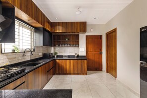 A modern kitchen with wooden cabinetry, a black countertop, and a tiled backsplash. - Aurum Heights by Red Olive (Bengaluru)
