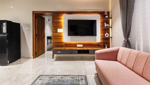 A modern living room with a flat-screen TV mounted on a wooden wall, a pink sofa, and a black refrigerator. - Aurum Heights by Red Olive (Bengaluru)
