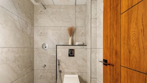 A bathroom with a toilet, shower, and wooden door. - Aurum Heights by Red Olive (Bengaluru)