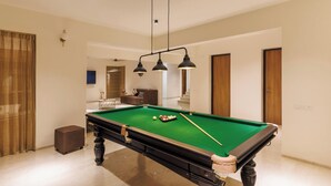 A pool table in a room with a modern design, a ceiling light fixture, and a door in the background. - Golfer's Arena by Stayjade (Hosur)