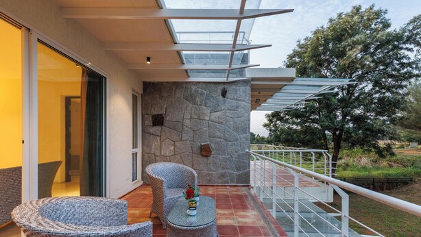 A balcony with wicker furniture, a stone wall, and a glass railing. - Golfer's Arena by Stayjade (Hosur)