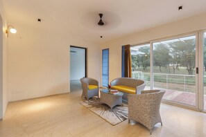 Amplia habitación con un gran ventanal corredero que da a un balcón, mobiliario de mimbre y ventilador de techo.