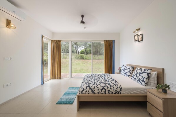 Un dormitorio con cama, mesita de noche, planta en maceta y vista al exterior a través de una puerta corrediza.