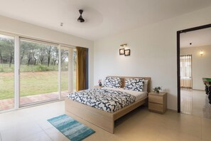 Un dormitorio moderno con una cama grande, una mesita de noche, una pequeña mesa y vistas al exterior a través de una puerta corrediza de vidrio.