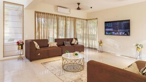 A modern living room with a brown sofa, a round coffee table, and a flat-screen TV mounted on the wall. - Golfer's Arena by Stayjade (Hosur)
