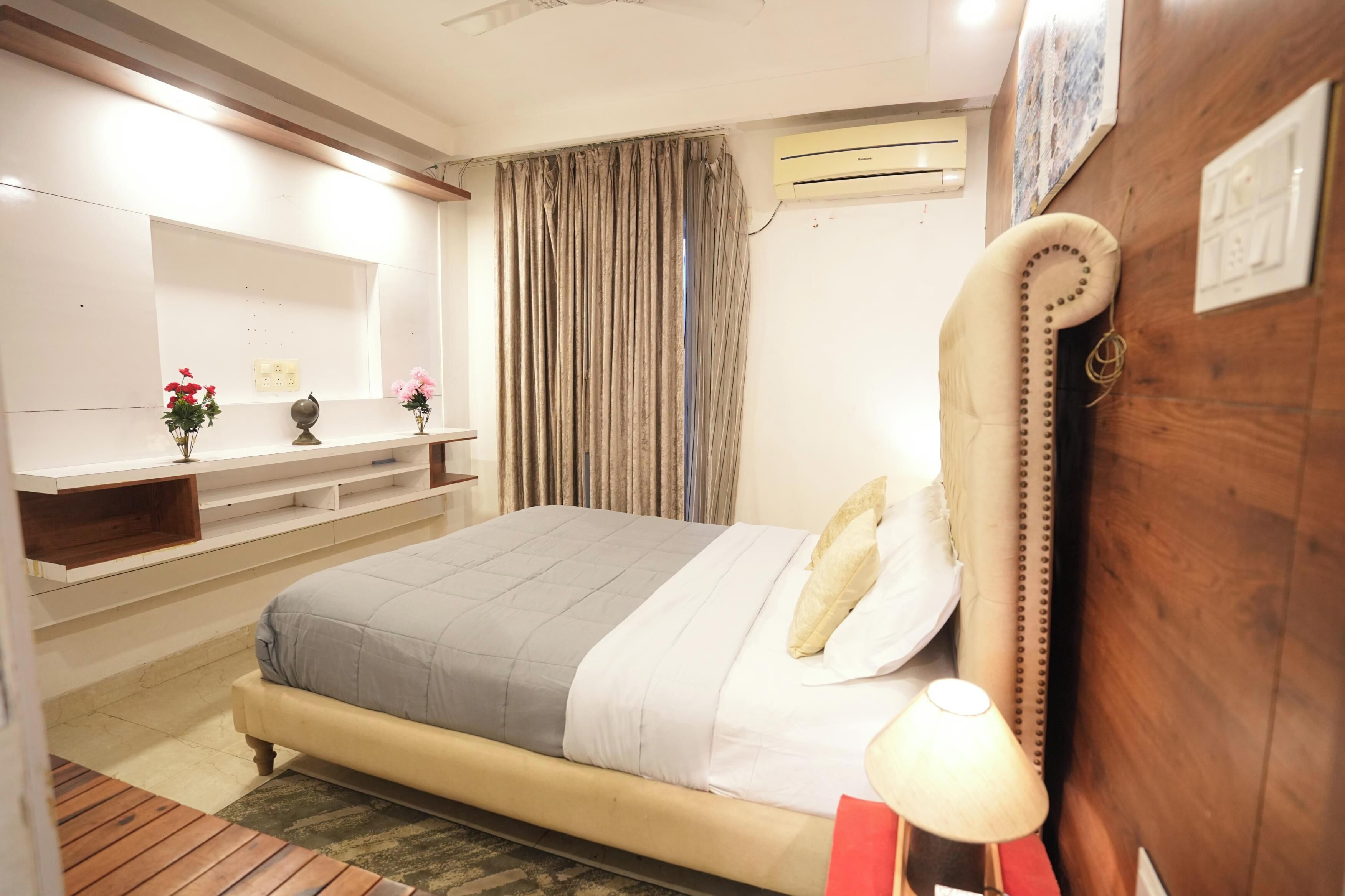 Un dormitorio con cama, mesita de noche, lámpara y unidad de aire acondicionado.