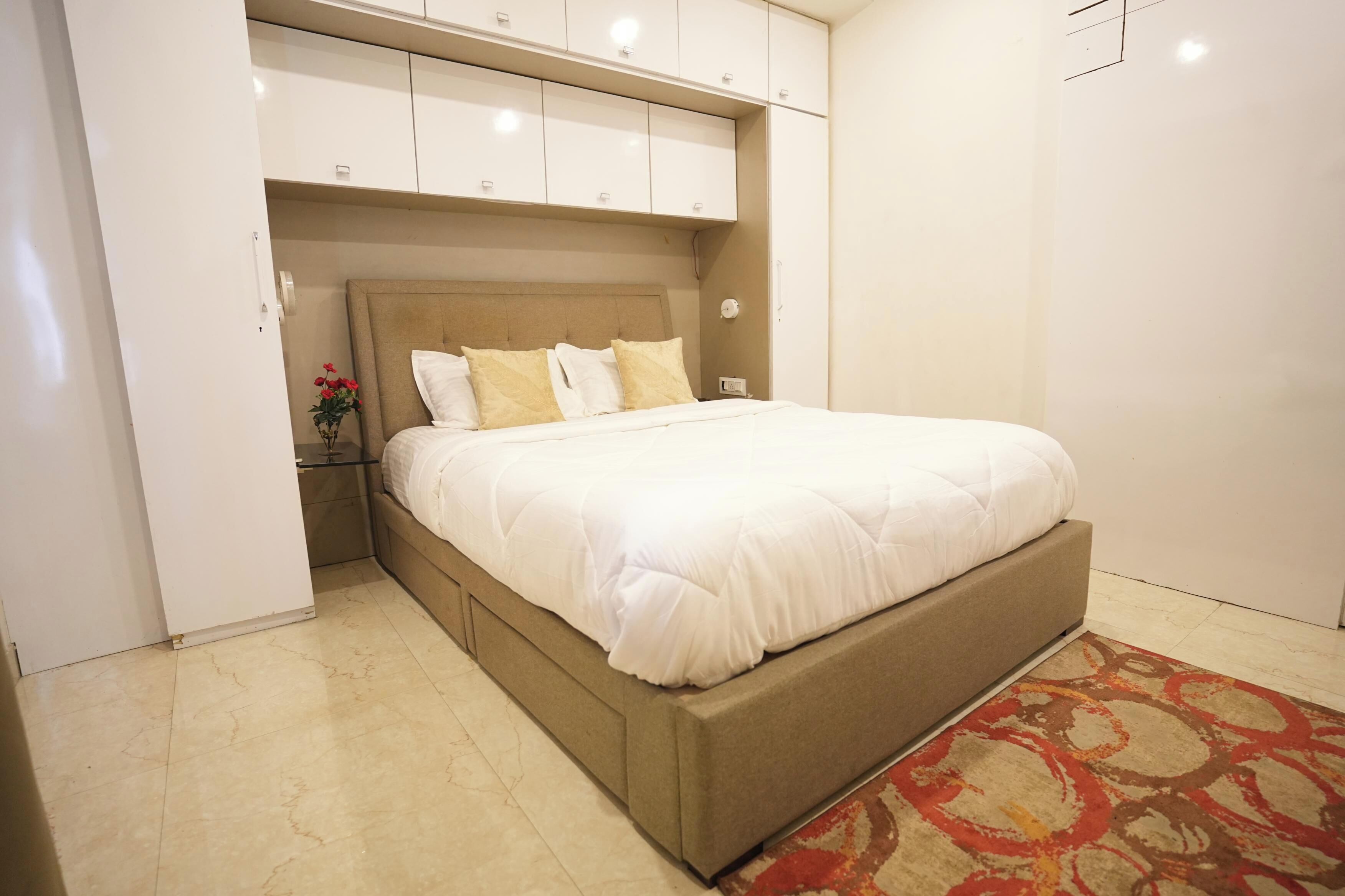 A bedroom with a bed, a nightstand, a vase with flowers, and a wardrobe.