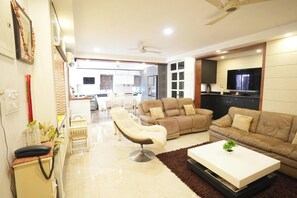 Un salon moderne avec un canapé, un fauteuil et une table basse. On y trouve également un téléviseur et un ventilateur de plafond.