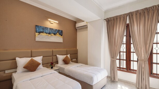 A hotel room with two beds, a painting on the wall, an air conditioning unit, and a window with curtains. - Emerald Apartments by Red Olive (Bengaluru)